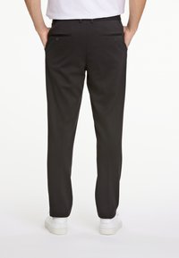 Schwarze Hosen mit tailliertem Schnitt, ausgestattet mit zwei Gesäßtaschen mit eleganten horizontalen Öffnungen und einer glatten Textur. Getragen mit weißen Sneakers.