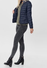 Giacca puffo navy con cuciture orizzontali, top verde oliva, jeans skinny neri e stivaletti neri con tacco ankle con un accento metallico.