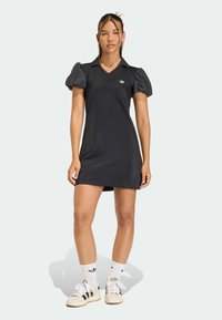 Czarna sukienka z krótkimi bufkami, dekoltem w serek i haftowanym logo na piersi. Do tego białe skarpetki oraz trampki z czarnymi paskami.