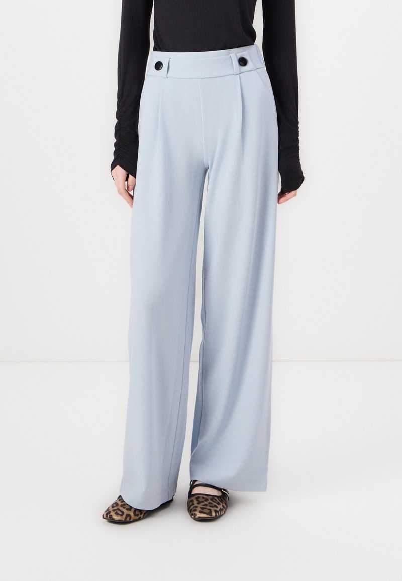 Pantalons larges bleu clair à taille haute, dotés de deux accents en boutons noirs et de plis à l'avant, associés à des chaussures plates à imprimé léopard.