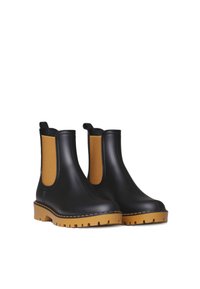 Bottes Chelsea noires en caoutchouc avec des panneaux élastiques beiges sur les côtés et des semelles texturées, dotées d'un bout arrondi et de languettes pour un enfilage facile.