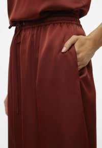 Bordeaux satijnen broeken met een elastische tailleband, voorzien van zijzakken en een gladde, glanzende textuur. Trekkoorddetail bij de taille.