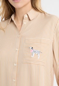 Beżowo-biała pasiasta koszula zapinana na guziki z haftowanym dalmatyńczykiem z różową obrożą na kieszeni piersiowej. Prosty kołnierzyk.