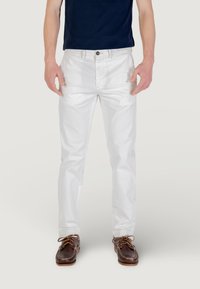 Pantaloni in cotone bianchi con gamba dritta, dotati di chiusura anteriore con bottone e tasche laterali, abbinati a scarpe da barca in pelle marrone.