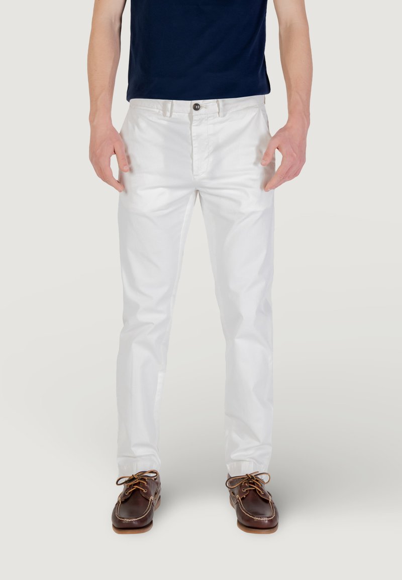 Pantaloni in cotone bianchi con gamba dritta, dotati di chiusura anteriore con bottone e tasche laterali, abbinati a scarpe da barca in pelle marrone.