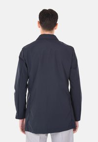 Giacca esterna blu navy con una texture liscia, maniche lunghe e colletto classico. Presenta un taglio dritto e dettagli minimi.