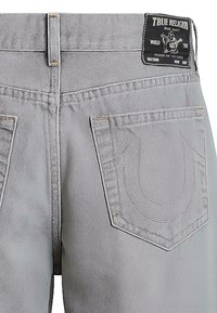 Szare dżinsy z klasycznym pięciopocketowym fasonem, widocznym szwem i metką w pasie. Tylnie kieszenie z charakterystycznym haftem logo.