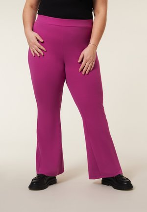 Flared broeken in felroze, met een rekbare stof, hoge tailleband en zwarte chunky schoenen. Gladde textuur zonder zichtbare patronen.