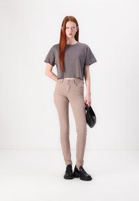 T-shirt gris cropped à manches courtes, jean skinny beige, chaussures noires à enfiler et sac à main noir, sur fond blanc.