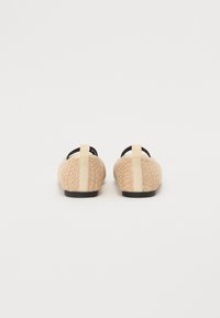 Μπεζ υφασμένα παπούτσια με μαύρες λωρίδες, επίπεδες μαύρες σόλες και μπεζ αξεσουάρ στην πλάτη. Υφασμάτινη επιφάνεια με ανάγλυφα σχέδια.