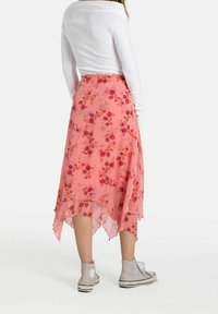 Rosa blommig kjol med en hög-låg nederkant och genomskinlig textur, prydd med små lila och röda blommor. Bärs tillsammans med en vit långärmad topp och grå sneakers.