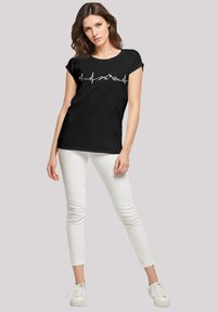 Zwarte katoenen T-shirt met een witte hartslaglijn graphic en bergsilhouetten. Gecombineerd met witte skinny jeans en witte sneakers.