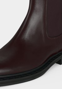 Bottine Chelsea en cuir marron foncé avec panneau latéral élastique et semelle noire avec bord texturé visible.
