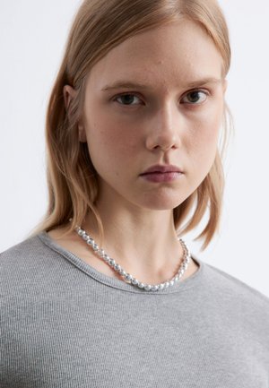 Gray ribbed top with a round neckline, worn with a silver pearl necklace. Background is plain white, focusing on the neckline and jewelry details.