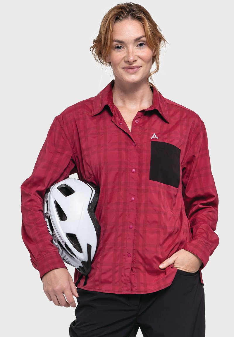 Rote karierte Langarmbluse mit einer schwarzen Brusttasche, Knopfleiste und pinken Knöpfen, gehalten neben einem weißen Fahrradhelm.