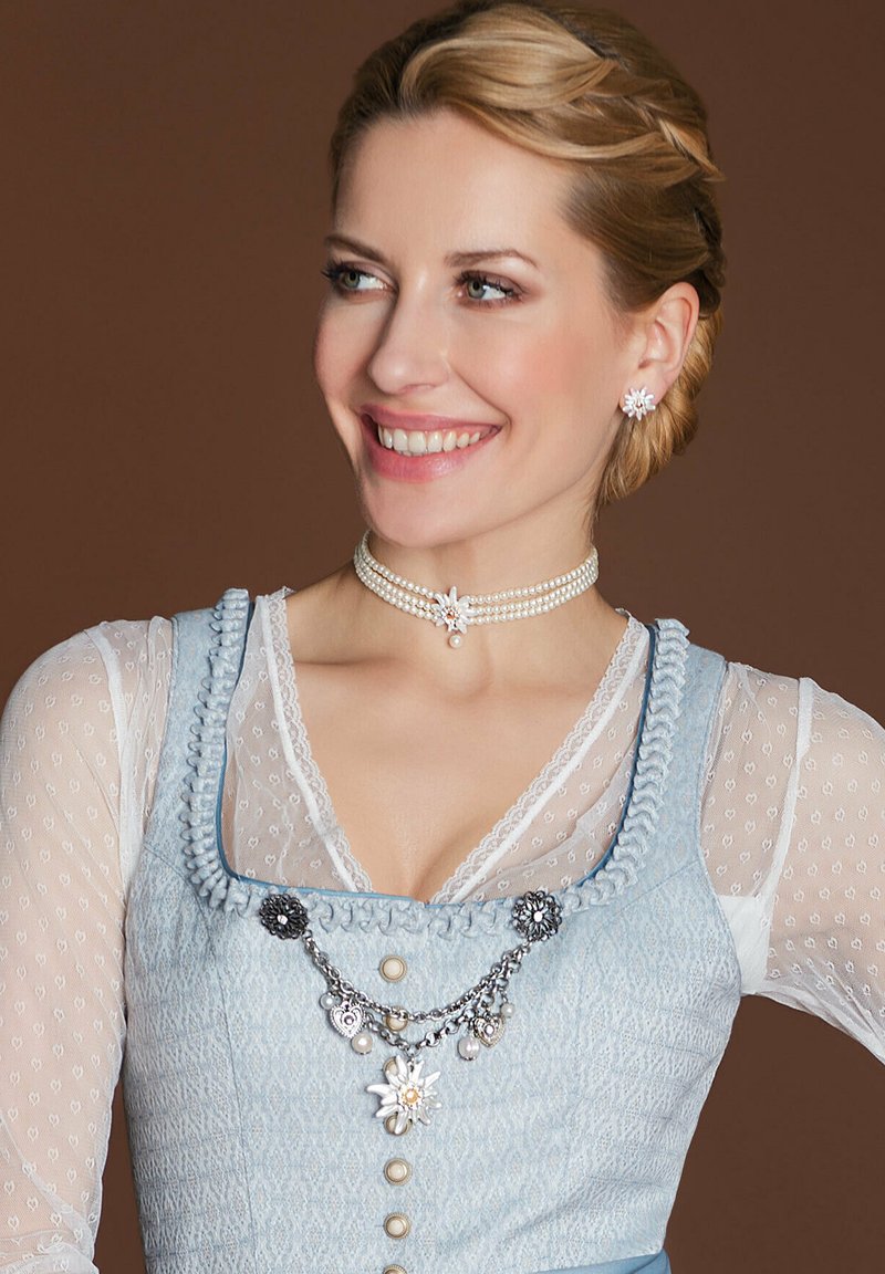 Hellblaues Dirndl aus strukturiertem Stoff, mit aufwendiger Raffung, weißen Spitzenakzenten und einer silbernen Kette mit floralen Details und Perlen.