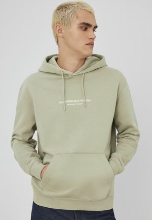 Hoodie vert clair avec une poche avant et un capuchon à cordon de serrage. Présente un texte blanc indiquant "JE SUIS UNE PERSONNE DU WEEK-END" sur la poitrine. Texture lisse.