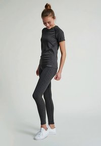 Dunkelgraues Sportshirt mit strukturierten Ärmeln, kombiniert mit Leggings mit Chevron-Muster. Beide haben eine eng anliegende Passform und elastischen Stoff.