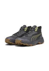 Scarpe sportive con una tomaia sintetica nera, lacci riflettenti, una suola spessa con una suola in gomma naturale e strisce verdi di accento.