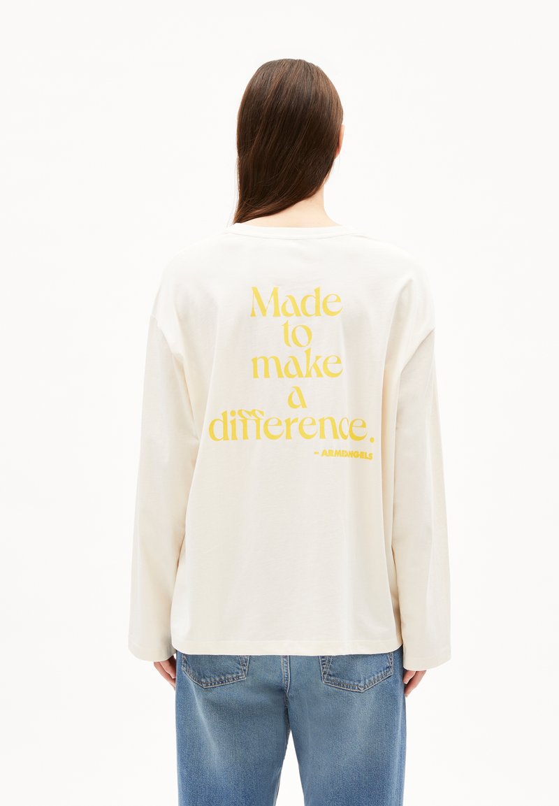 Lange mouw off-white t-shirt gemaakt van katoen, met gele tekst op de achterkant: "Gemaakt om een verschil te maken." Ronde hals en ontspannen pasvorm.
