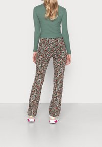 Uitlopende leggings met een zwart bloemenpatroon, versierd met kleine witte, rode en groene bloemen, gecombineerd met een aansluitend groen shirt met lange mouwen.