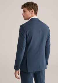 Mörkblå kavaj i slätt tyg, med en ventil, slim fit och fyraknappar på ärmarna. Modellen visas från baksidan.