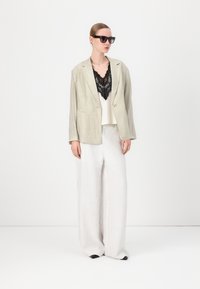 Light grey linen blazer over a white lace camisole, paired with wide-legged white textured pants and black sunglasses.