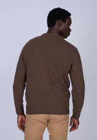 Pull en tricot marron avec un col et des poignets côtelés, présentant une finition texturée. Porté avec un pantalon kaki, vu de dos.
