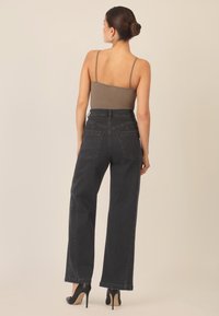 Dunkelblaue High-Waist-Jeans mit weitem Bein, ausgestattet mit Gesäßtaschen und einem glatten, leicht strukturierten Stoff. Kombiniert mit einem hellbraunen Oberteil.