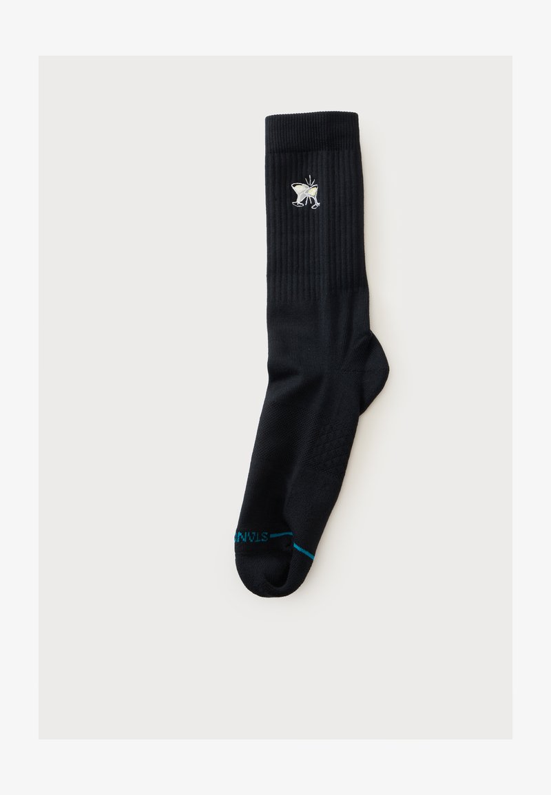 Chaussette noire à tige côtelée, papillon blanc brodé près du sommet, et petit texte bleu sur la zone des orteils sur fond clair.