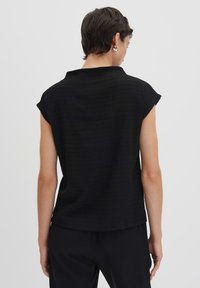 Schwarzes, strukturiertes Kurzarmoberteil mit Kragen, das ein geripptes Muster und eine lässige Passform aufweist, kombiniert mit schwarzen Hosen.