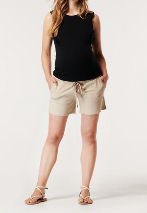 Top nero senza maniche con dettagli arricciati, abbinato a pantaloni beige con vita elastica e cordino. Sandali piatti completano il look.