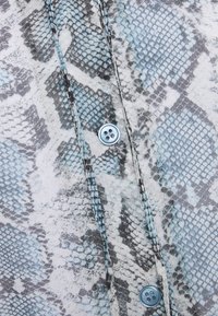 Knappert skjorte med et blåt og gråt slangemønster. Stoffet har en glat overflade, med en lyseblå knap og kontraststing.