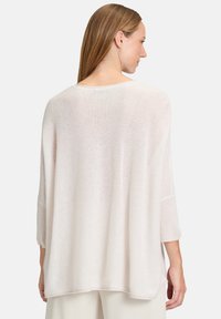 Pull en tricot rose clair avec une coupe décontractée, des manches trois-quarts et un ourlet côtelé. Texture douce et tissu légèrement transparent.