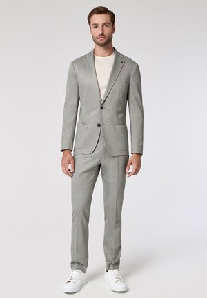 Gray tailored suit with notched lapels and two front pockets; worn with a white T-shirt and white sneakers, creating a modern look.