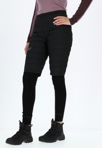 Black insulated shorts layered over black leggings, featuring a smooth texture, padded design, and a side logo detail. Completed with black boots.