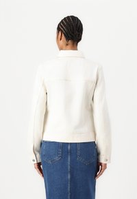 Hvit denimjakke med lange ermer, kragehals og rett nederkant. Har sømdetaljer og knappede mansjetter.