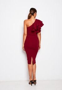 Burgunderfarbenes, figurbetontes Midikleid mit einem abgeknöpften Schulterriemen, das mit einem großen Rüschenelement verziert ist. Der Schlitz reicht bis zur Mitte des Oberschenkels, das Material hat eine glatte Textur und das Design ist elegant.