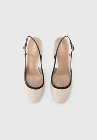 Μπεζ παπούτσια slingback με μαύρη επένδυση, λεία υφή, διάτρητη εσωτερική σόλα και ελαφρύ τακούνι. Λεπτομέρεια μεταλλικής αγκράφας στο λουράκι.