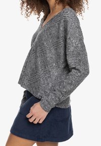 Pulóver gris de punto texturizado con cuello en V y mangas largas, combinado con una falda de pana azul marino que presenta dos bolsillos frontales. Etiqueta del logo de Roxy visible.