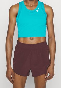 Turquoise cropped sporttop met een wit Nike-logo, gecombineerd met bordeauxrode sportshorts met een elastische tailleband en zijzakken.