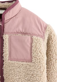 Kurtka polarowa z kremowym, teksturowanym korpusem, kontrastującym różowym panelem na ramionach oraz pasującą kieszenią. Posiada wysoki kołnierz i zamek błyskawiczny.
