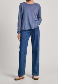 Světle modrá košile s dlouhým rukávem a volným střihem, v kombinaci s tmavě modrými džíny s rovnými nohavicemi a světle růžovými teniskami s hnědou podrážkou.