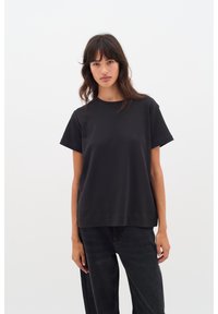 Mustast puuvillasest materjalist lühikeste varrukatega t-särk, ümara kaelusega ja lõdva istuvusega. Sile tekstuur ja lihtne disain ilma mustrite või aktsentideta.