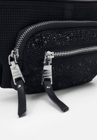 Černá texturovaná kabelka se dvěma zipovými přihrádky, zdobená černými krystaly. Obsahuje kovové doplňky a kožené popruhy.