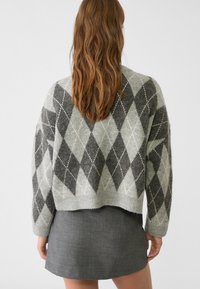 Grauer Wollmischpullover mit einem Argyle-Muster in Dunkelgrau und Hellgrau, kombiniert mit einem strukturierten grauen Minirock. Kürzes Design.