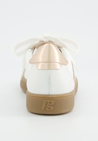 Baskets blanches avec semelle beige et languette dorée métallique, présentant des lacets blancs noués en nœud, vues de derrière.