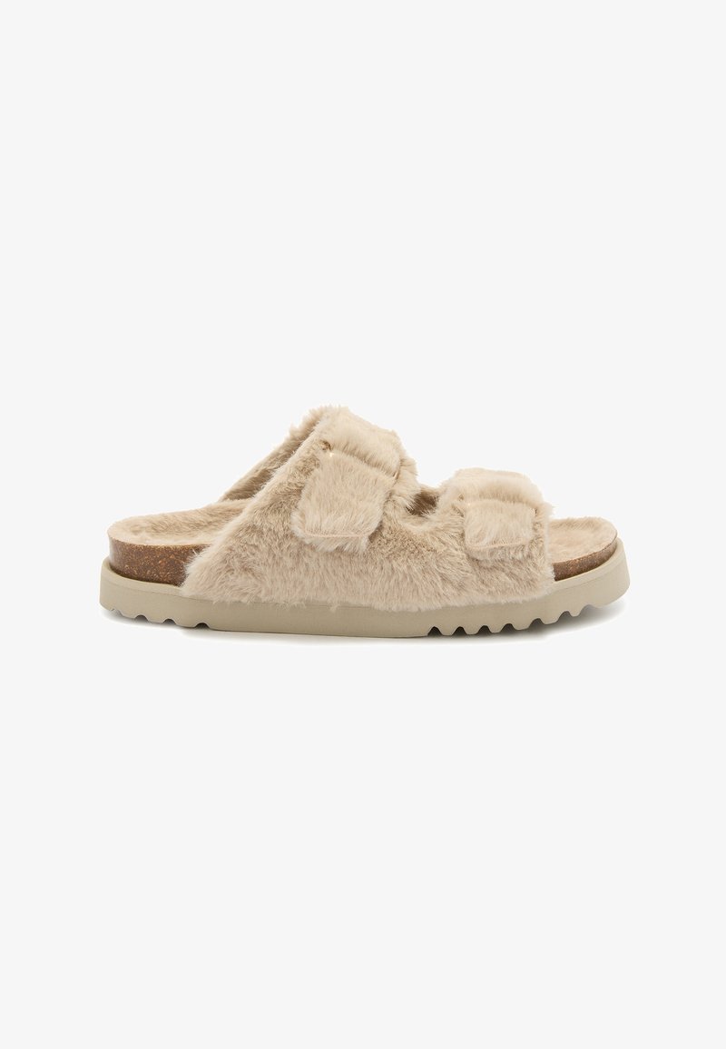 Sandale à glissière en fausse fourrure beige avec deux sangles réglables, semelle en liège, semelle en caoutchouc texturée et forme arrondie.