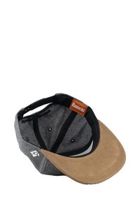 Gray and brown cap with a suede peak, black interior, and a brown leather tag marked "Pumuckl." Features sewn ventilation holes.