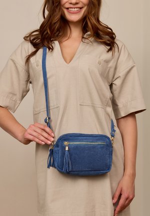Blaues Wildleder-Crossbody-Tasche mit goldenen Beschlägen, einer Reißverschlusstasche und Quastenakzenten. Kompakte rechteckige Form mit einem Schulterriemen.